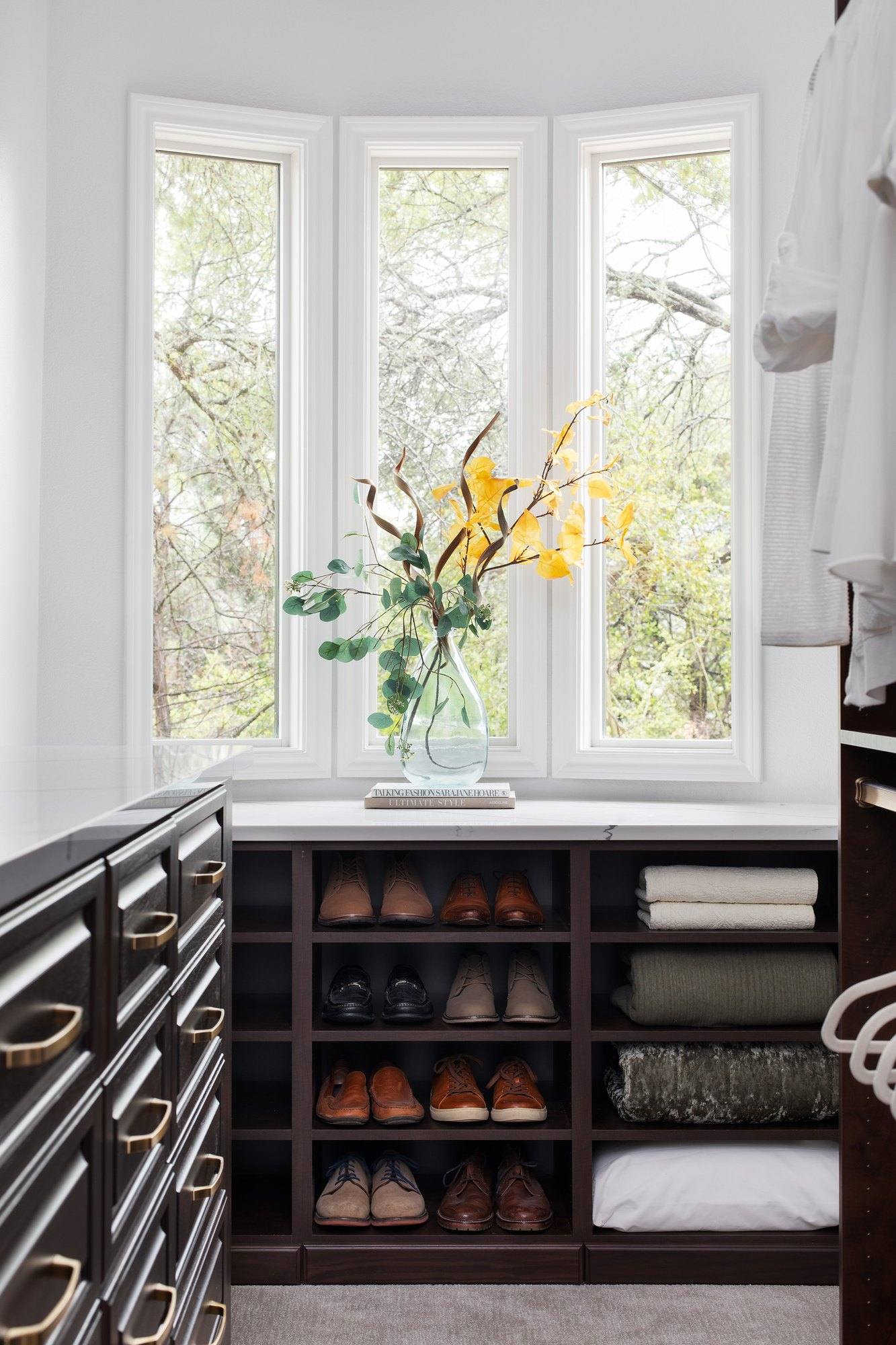 Dark-finish closet section under a bay window with shoe cubbies, folded linen shelves and a column of drawers
