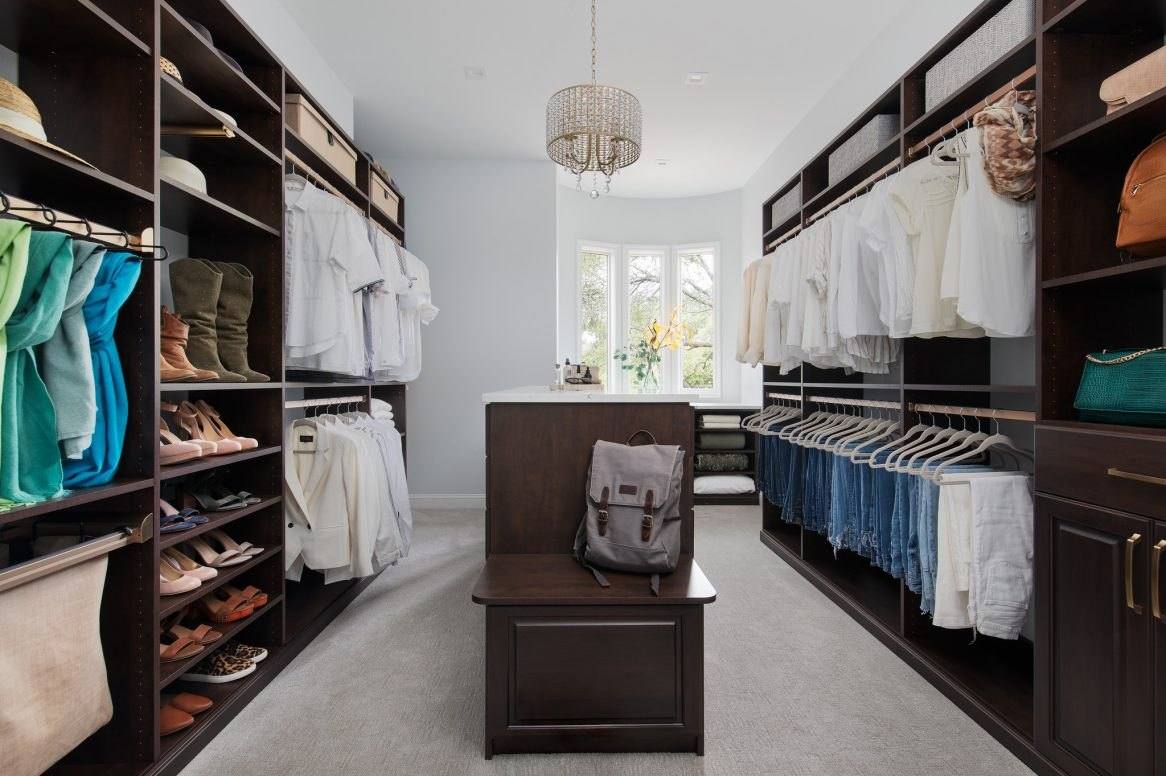 Walk-in closet in a dark wood finish with a center island bench, cubbies for shoes and folded clothes, and double hanging
