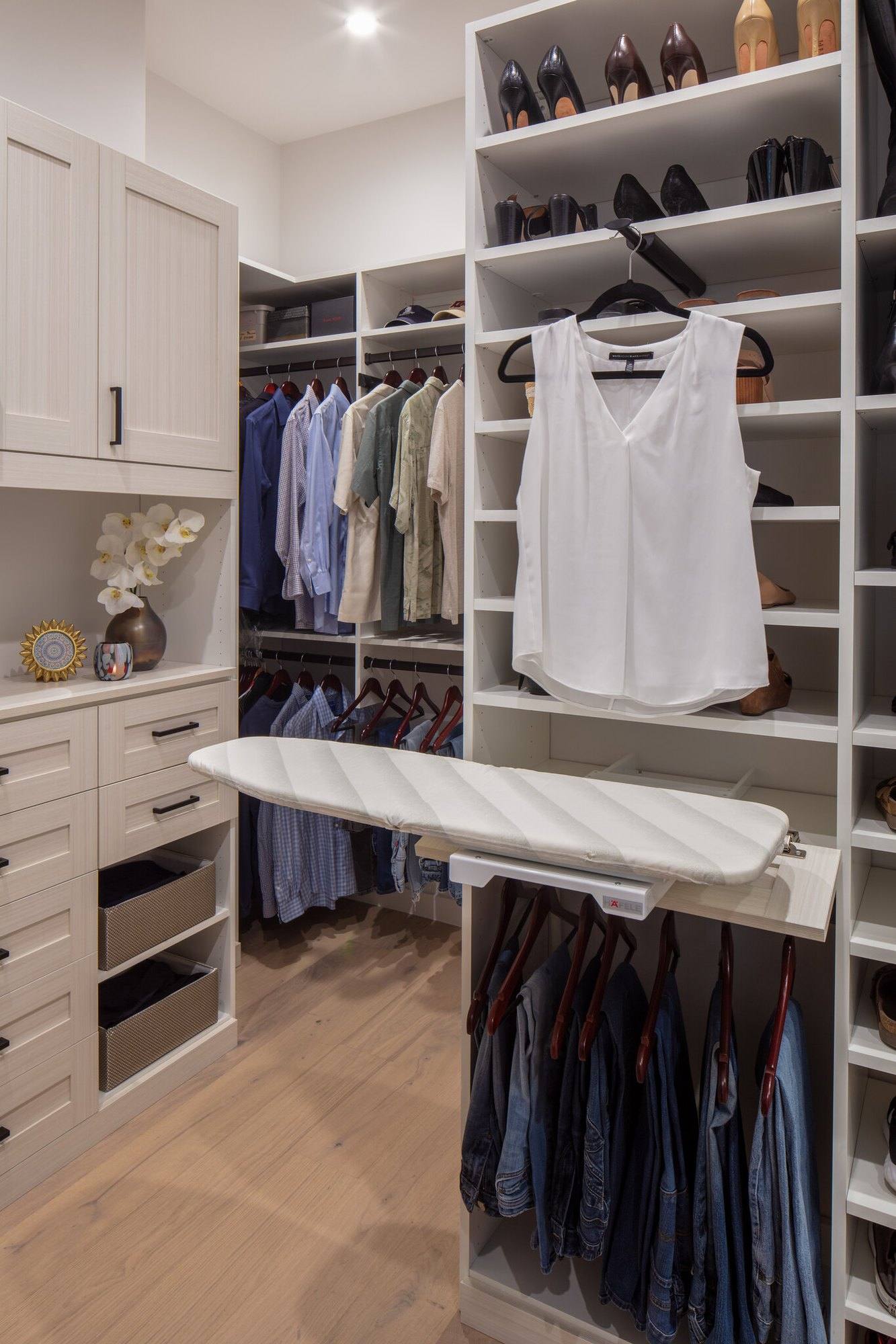 White walk-in closet with a fold-out ironing board, drawers, shoe shelves and hanging sections