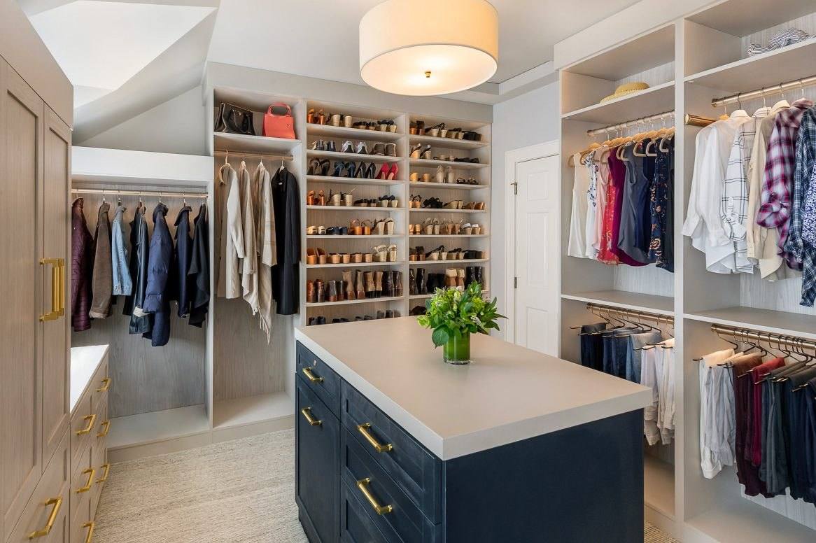 Walk-in closet with white shelving, a tall shoe wall and a navy blue island with a light stone top