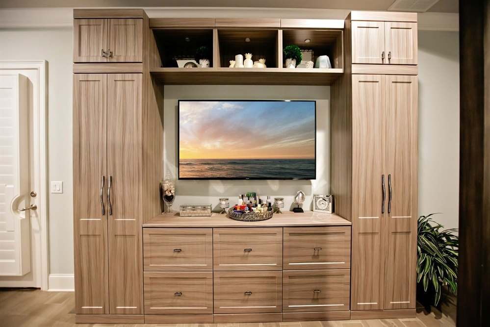Wood-tone entertainment wall unit with tall cabinets on each side of a television, open shelving and lower drawers