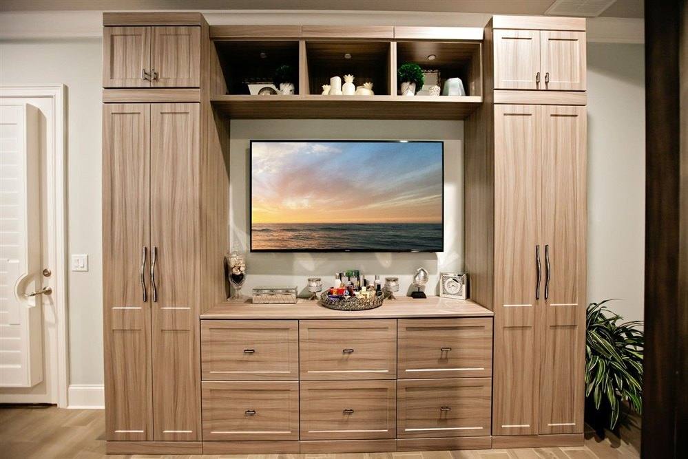 Wood-tone entertainment wall unit with tall cabinets on each side of a television, open shelving and lower drawers