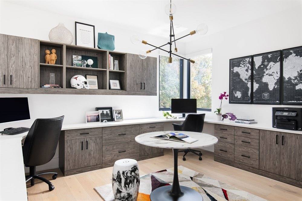 Home office with gray wood-grain desks, open shelving and cabinets along two walls and a small round meeting table
