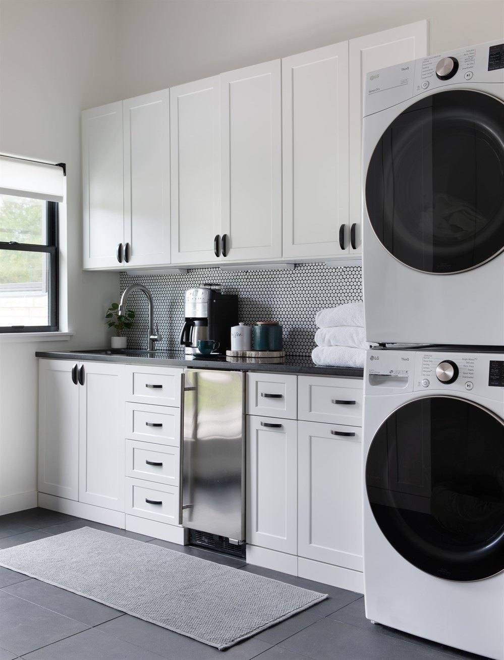 White laundry room with stacked washer and dryer, upper and lower cabinets and a countertop
