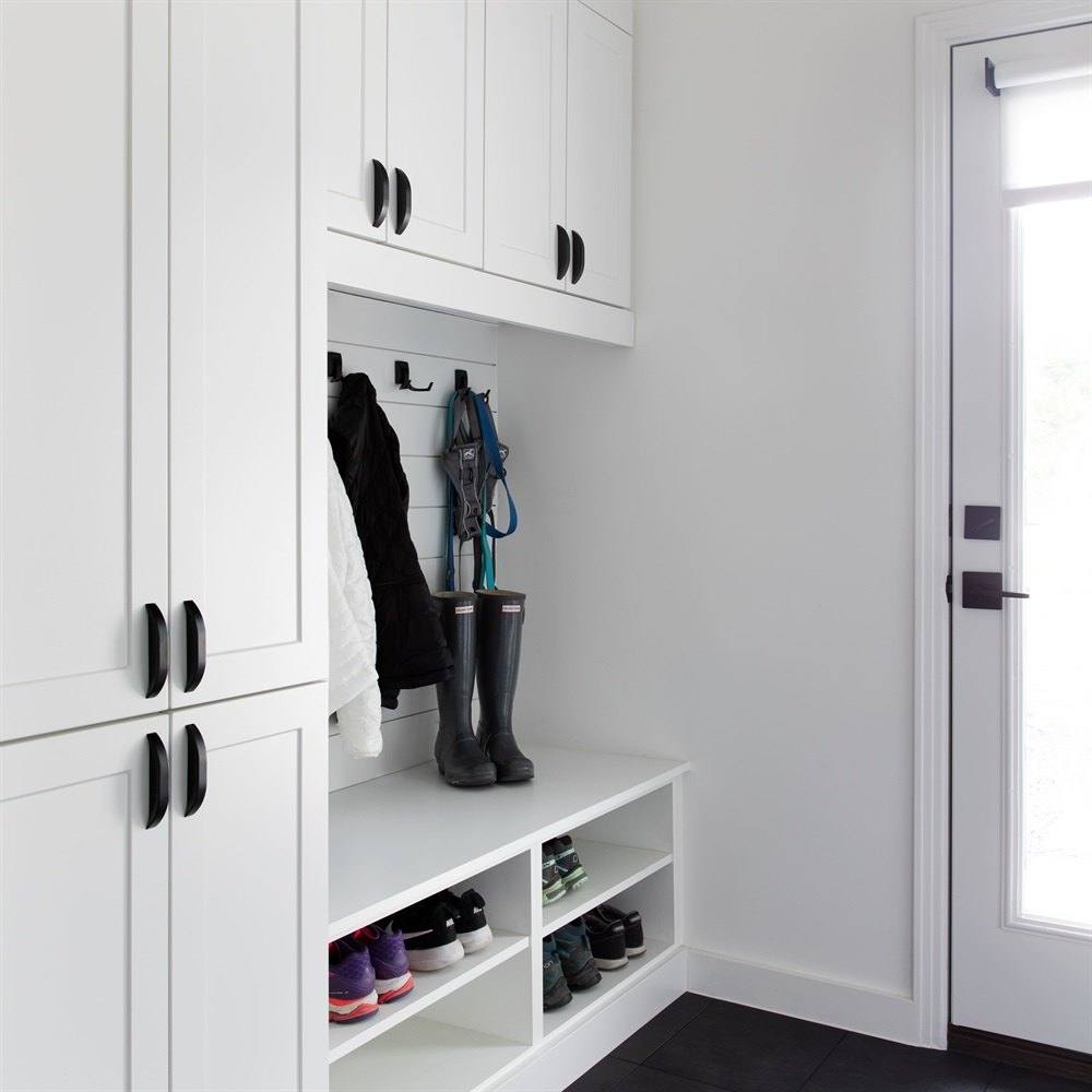 White mudroom unit with a tall cabinet, coat hooks, a bench and open shoe cubbies beside an exterior door