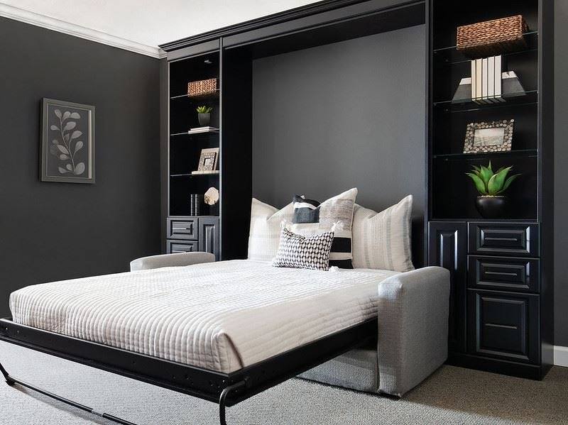 Open Murphy bed with a dark panel finish, flanked by bookshelves and cabinets