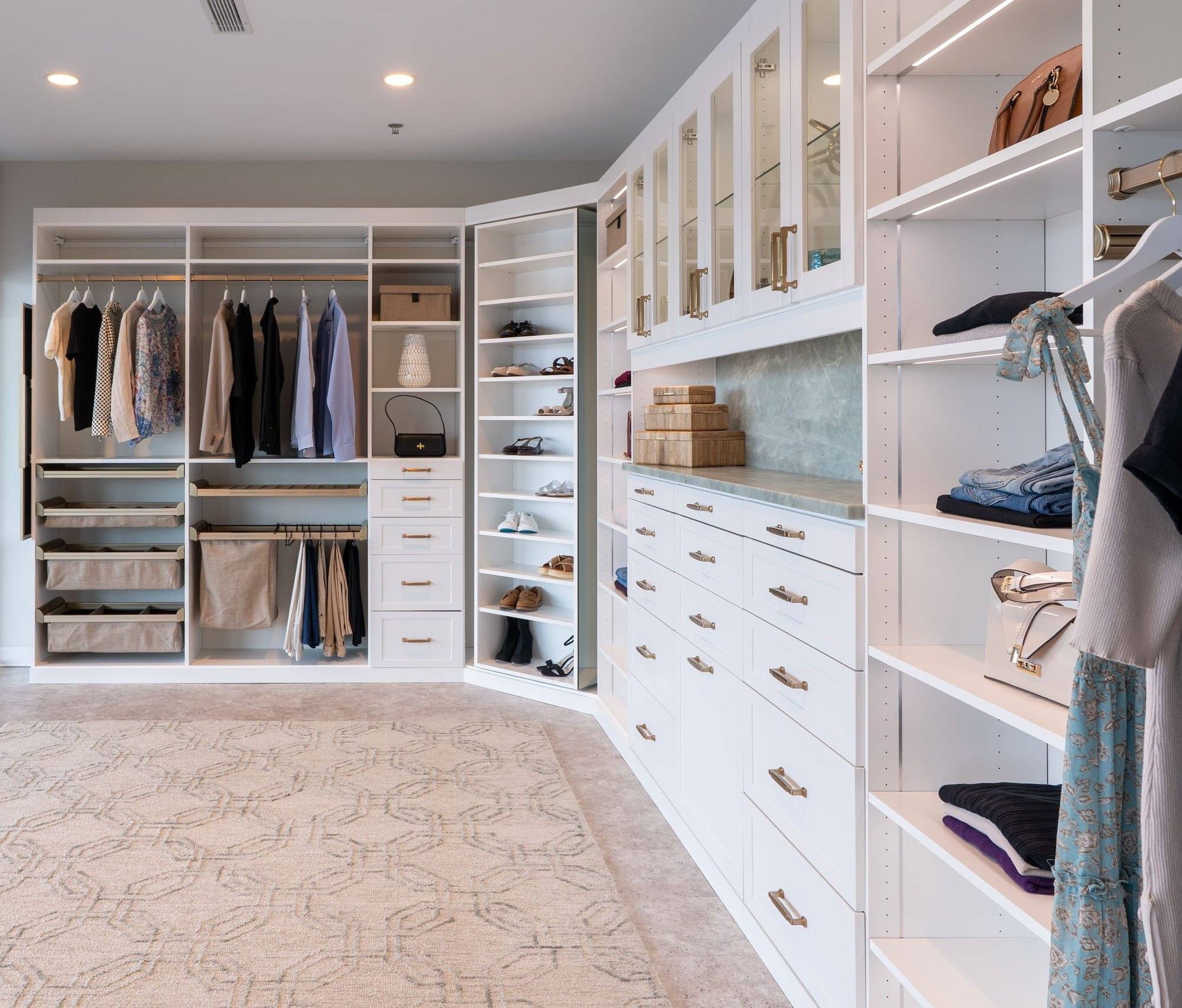 Corner of the showroom closet display with double hanging rods, pull-out fabric bins, an angled shoe tower and white drawers with brass pulls