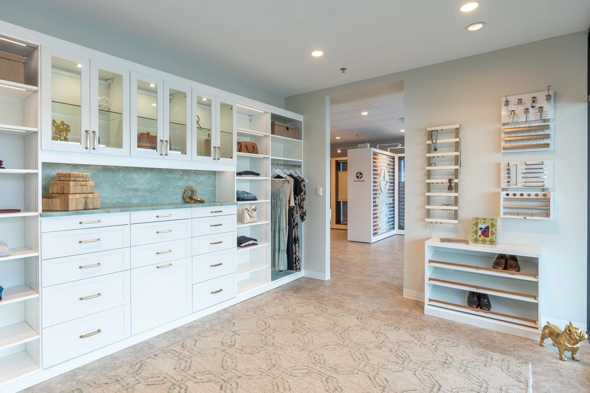 Closet display at the Hanover Center showroom with glass-front upper cabinets, a wall of white drawers, open shelving, hanging space and hardware sample boards