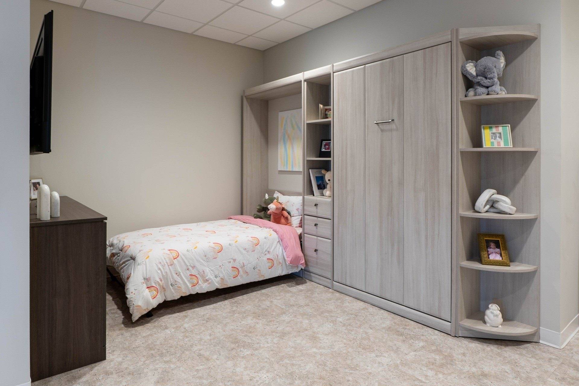 Murphy bed display in the showroom, folded down and made up, framed by side cabinets and curved corner shelving in a light gray wood-grain finish